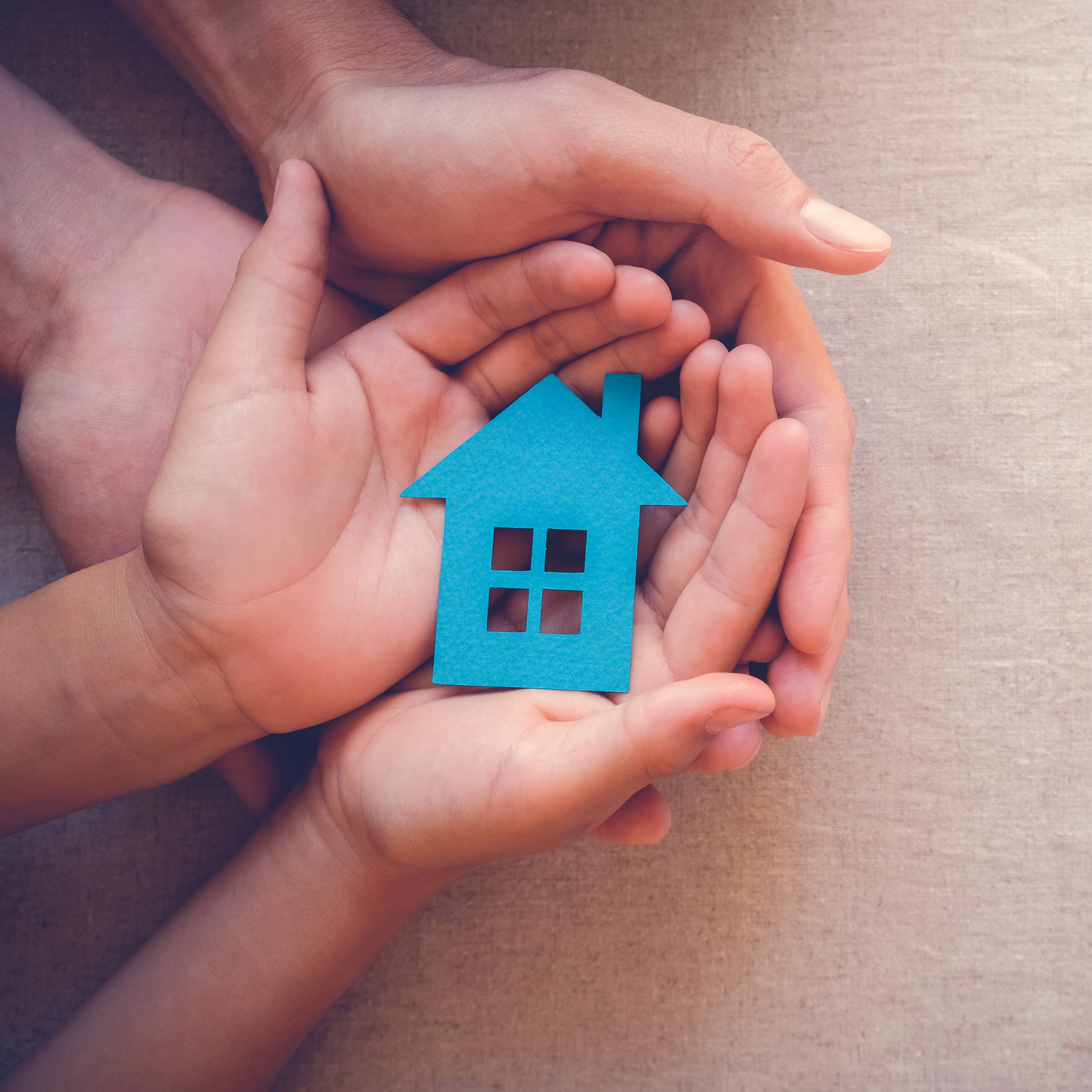 Adult and child hands holding paper house, family home and real estate concept